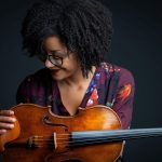 A woman poses looking at her viola.