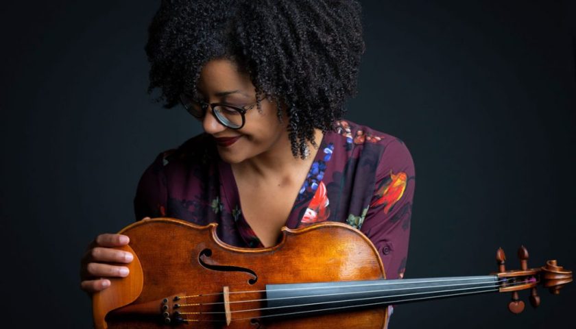 A woman poses looking at her viola.